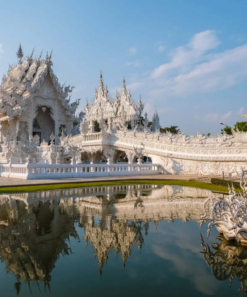Il Wat Rong Khun (Tempio Bianco) a Chiang Rai, Thailandia, con le sue elaborate architetture bianche e scintillanti che si riflettono splendidamente in uno specchio d'acqua